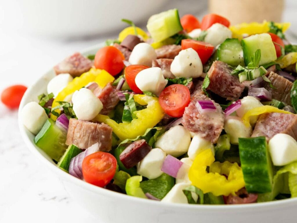 Italian salad with cherry tomatoes, cucumbers, mozzarella balls, salami, red onions, and banana peppers.