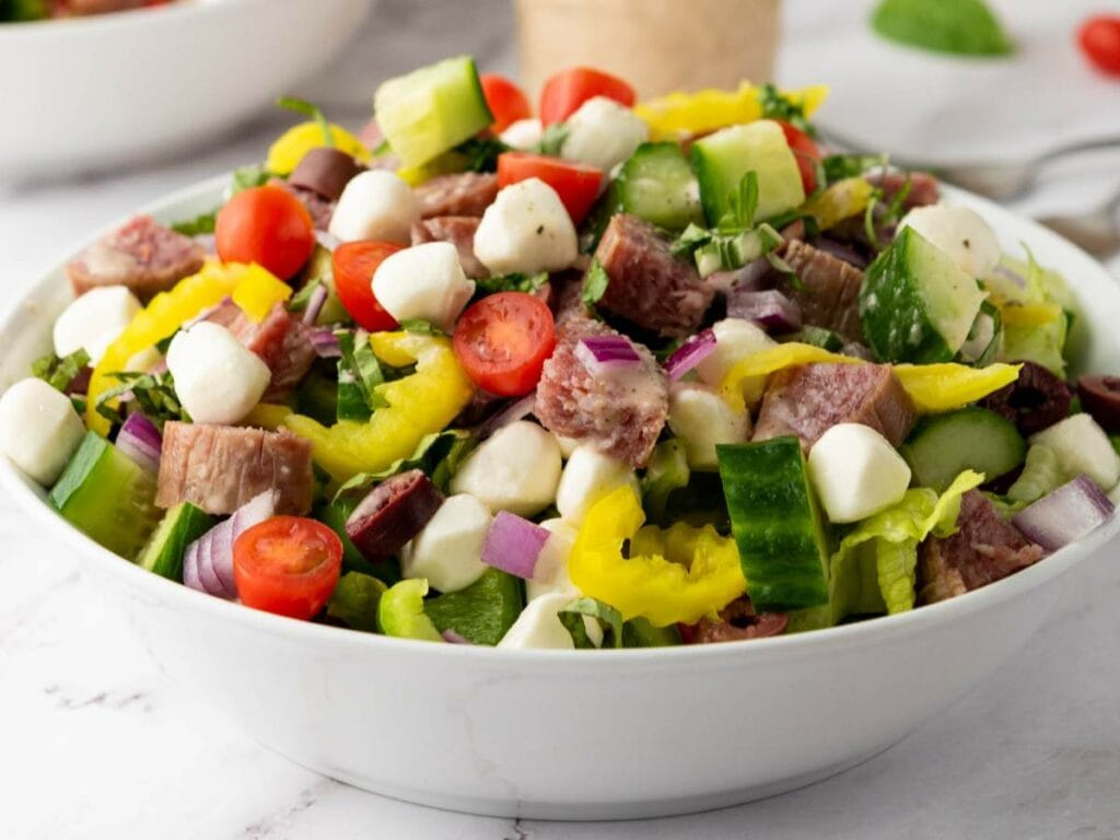 A italian salad containing sliced cucumber, cherry tomatoes, red onion and other ingredients.
