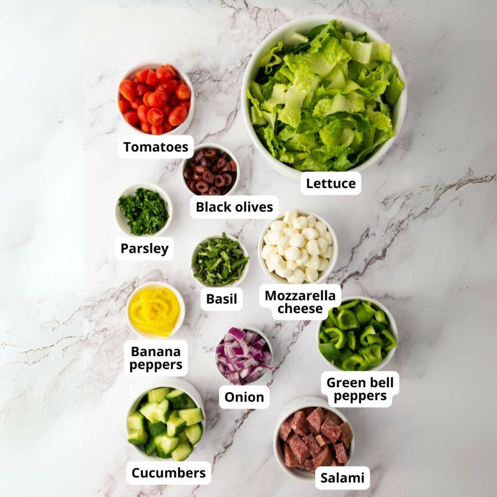 A variety of salad ingredients in bowls on a marble surface.