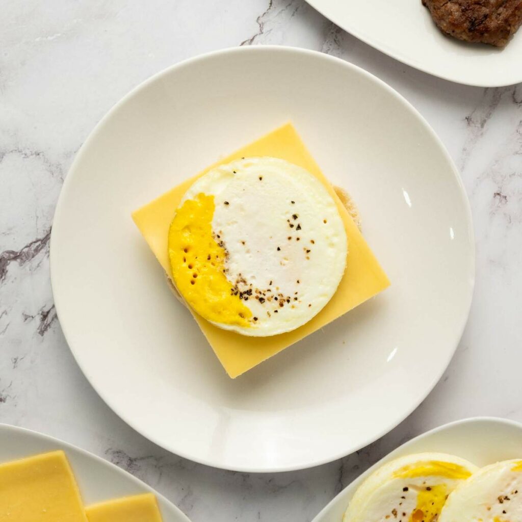 A cooked round egg with pepper sits on a slice of cheddar cheese on a plate, viewed from above.