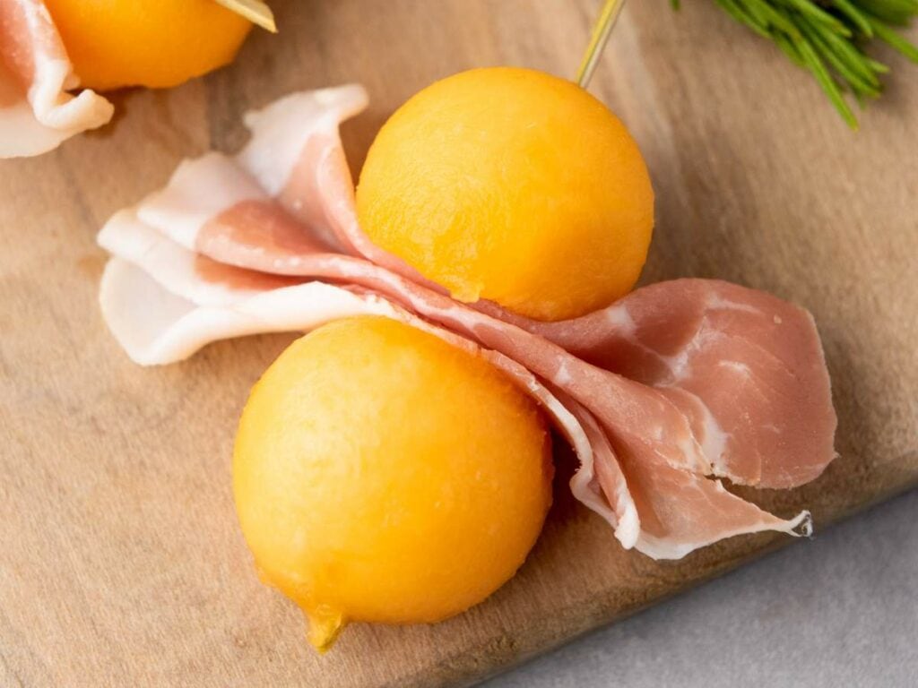Two melon balls are skewered together and placed on a wooden surface.