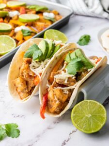A chicken fajitas in a tortillas on a marble surface next to a pan of the same fajitas.