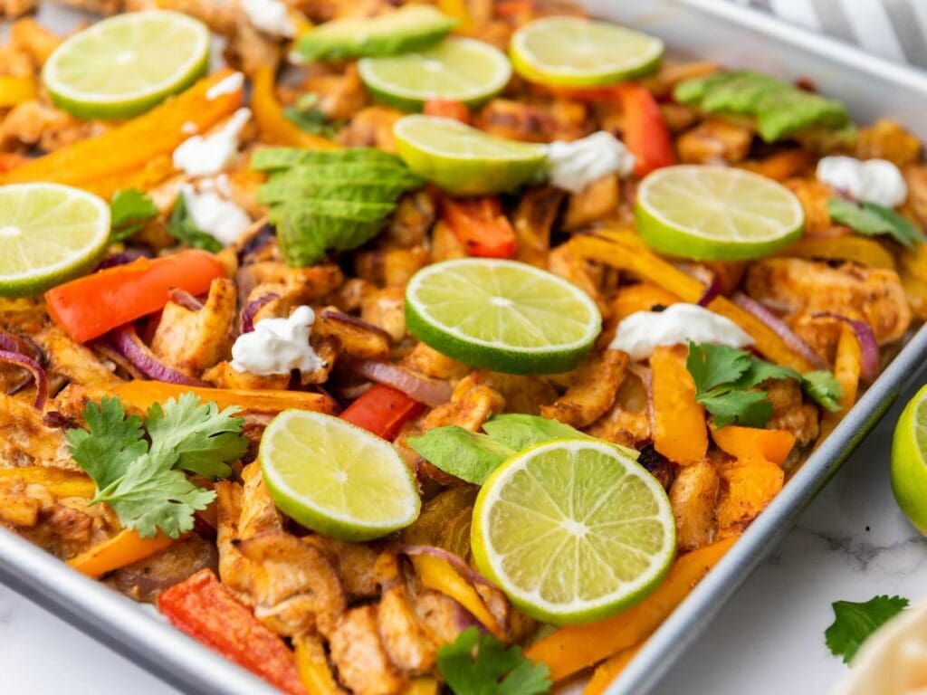 Half-view of sheet pan chicken fajitas garnished with fresh cilantro on a white marble surface.