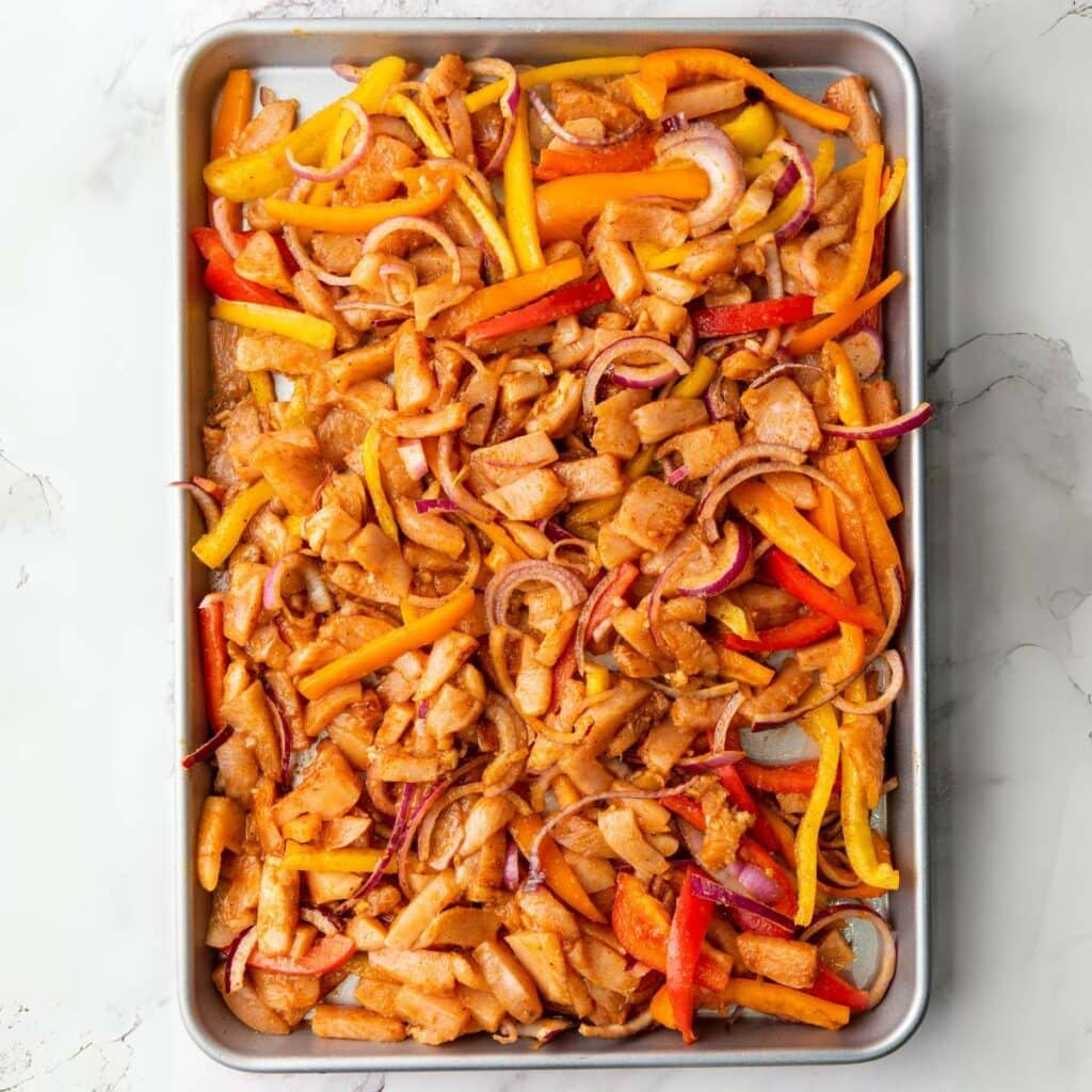 Seasoned chicken with herbs and spices arranged on a baking pan a marble surface ready to bake.