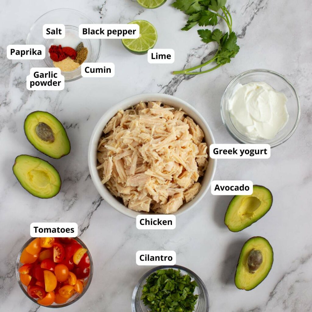 A bowl of labeled ingredients of simple chicken salad recipe on a marble surface.