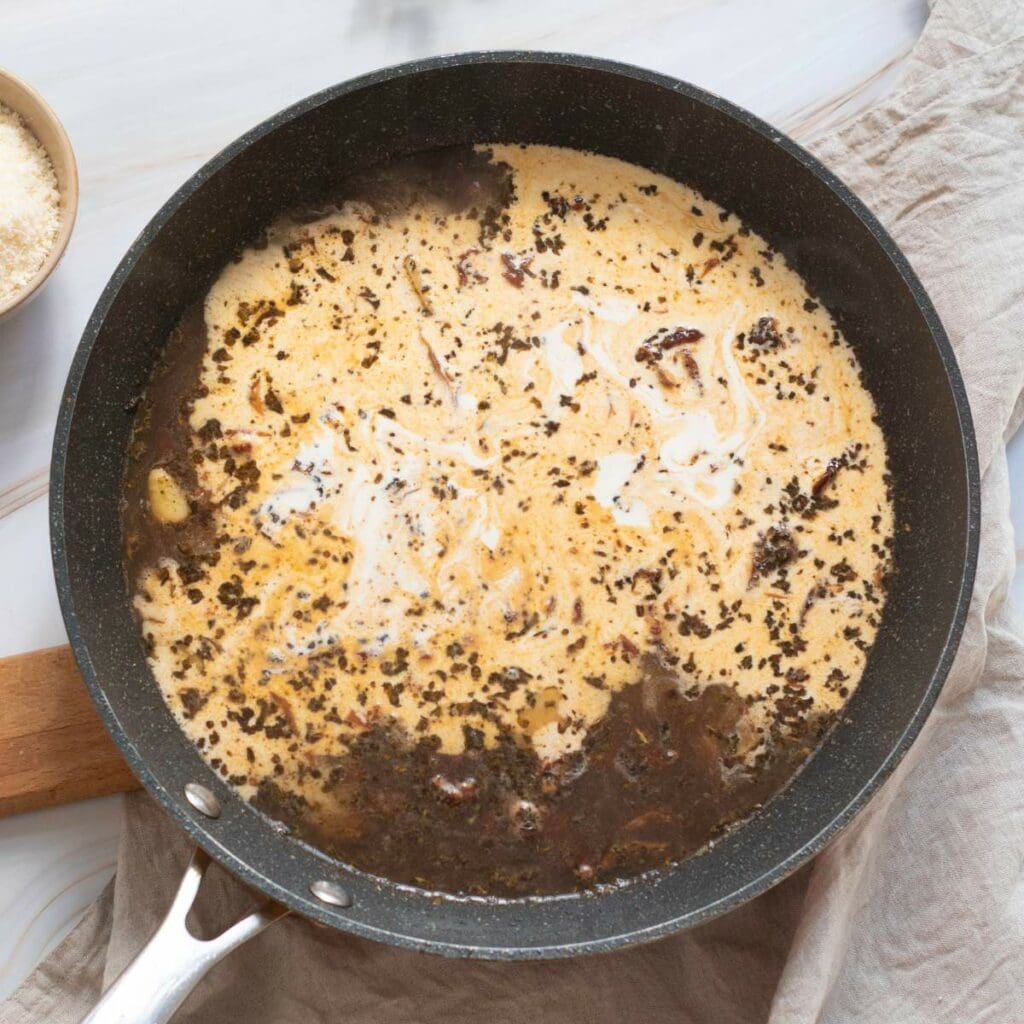 Brown and white liquid are mix in the black skillet on a white wooden surface.