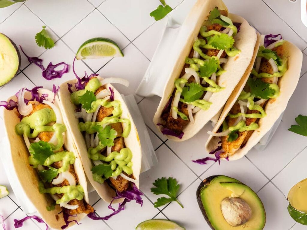 Tilapia tacos filled with grilled meat, shredded cabbage, onions, cilantro, and green sauce.