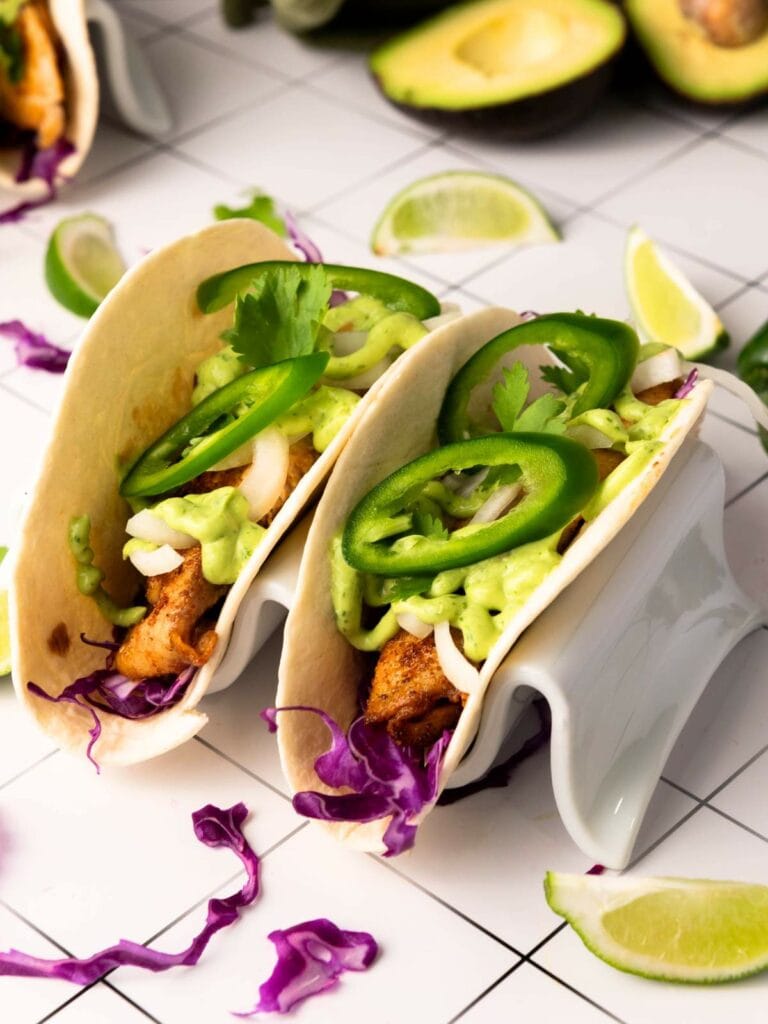 Two tilapia taco, filled with grilled fish, sliced jalapeños, avocado sauce and other ingredients.