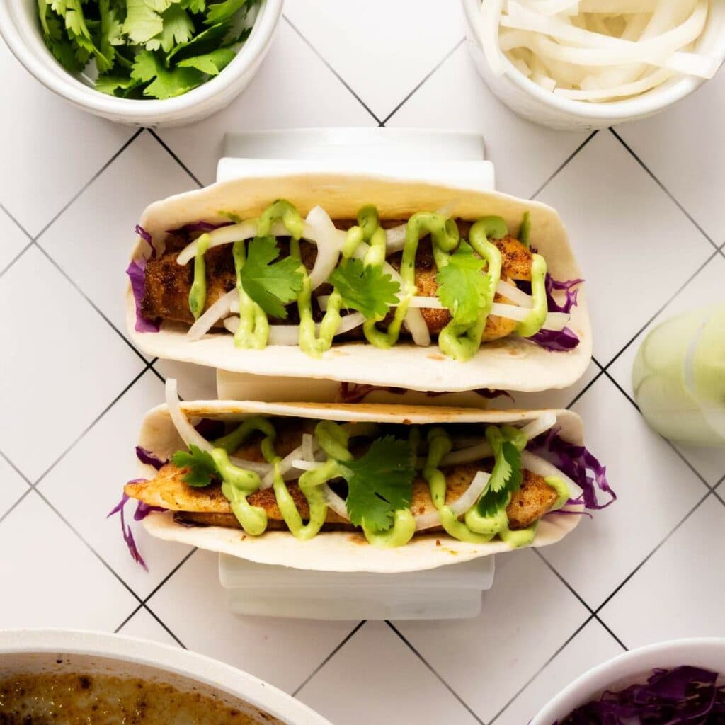 Two fish tacos topped with sliced onions, green sauce, and cilantro.