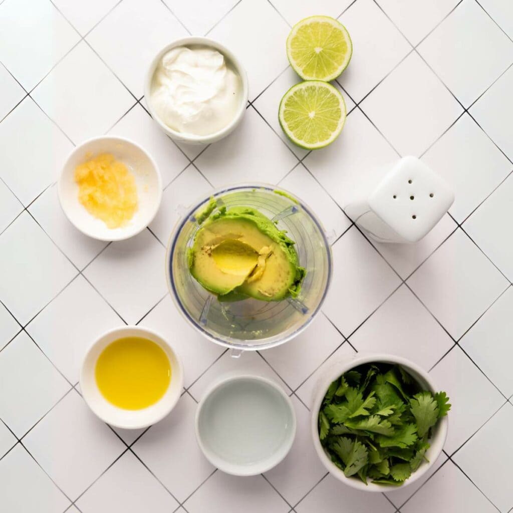A top-down view of avocado, cilantro, lime, yogurt, olive oil, garlic, and salt.