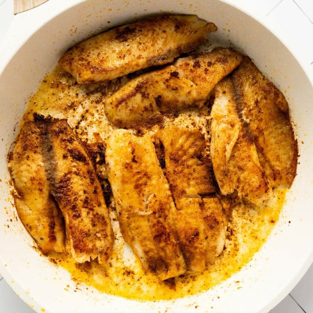 Pan of seasoned fish fillets being cooked in a creamy, buttery sauce.