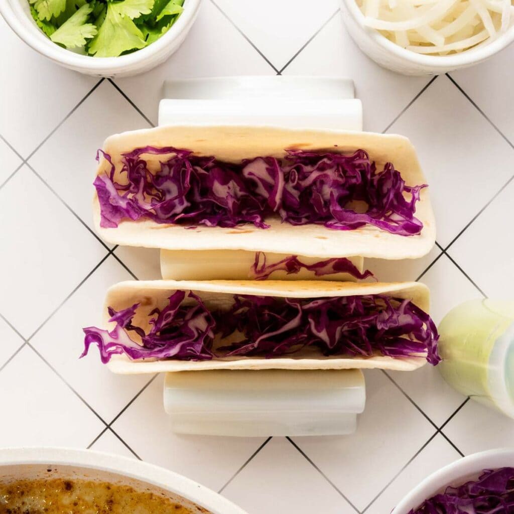 Two soft tacos filled with shredded purple cabbage on a white tiled surface.