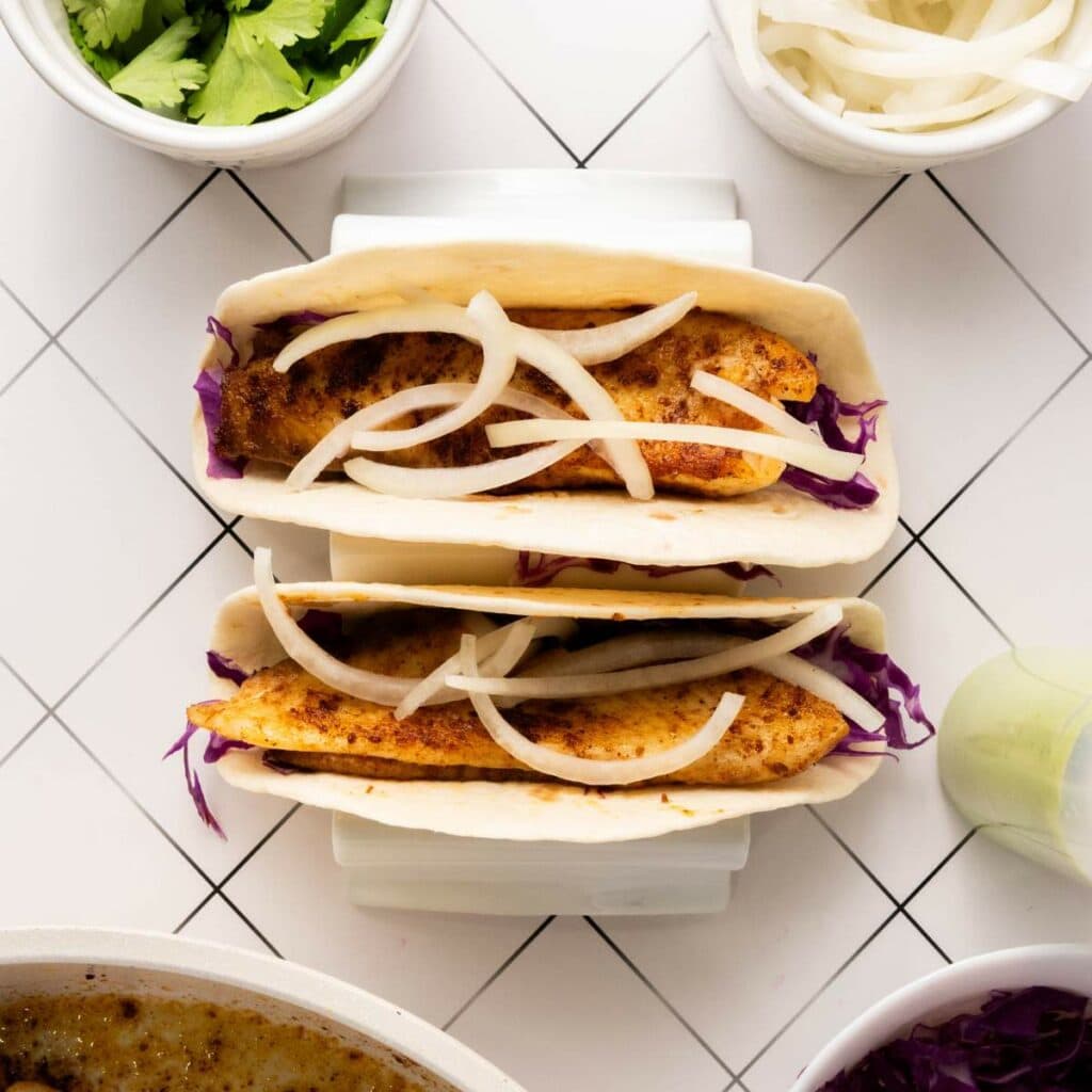 Two fish tacos in soft tortillas with shredded cabbage and sliced onions.