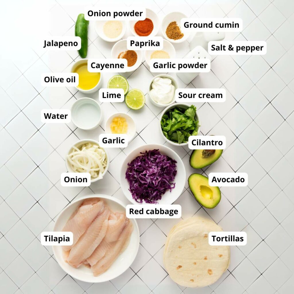 Labeled ingredients for tilapia tacos are arranged on a white tiled surface.