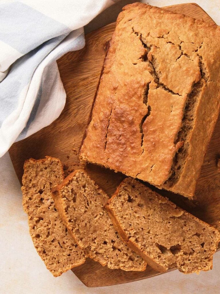 A loaf of bread with a cracked top sits on a wooden cutting board, partially sliced.