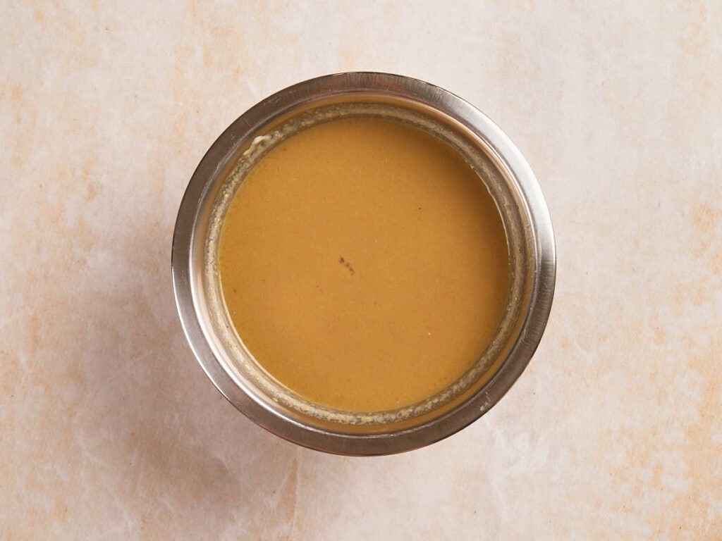 A stainless steel bowl filled with yellow-brown liquid, viewed from above, on a light-colored surface.