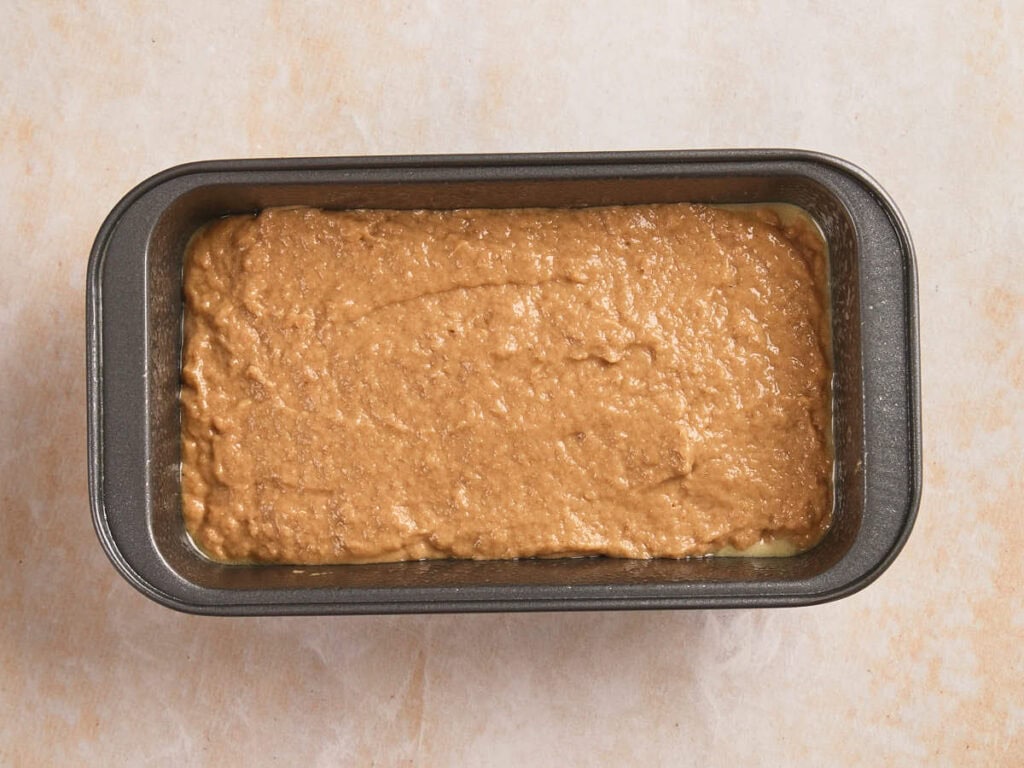 A loaf pan filled with unbaked brown batter placed on a light-colored surface.