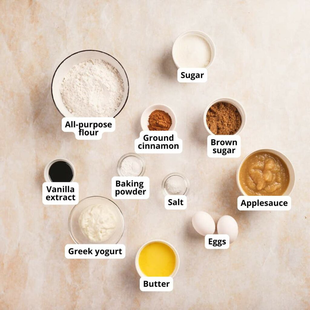 Labeled baking ingredients for applesauce bread recipe on a light surface.