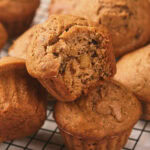 A close-up of several nut muffins on a cooling rack, with one muffin partially eaten.