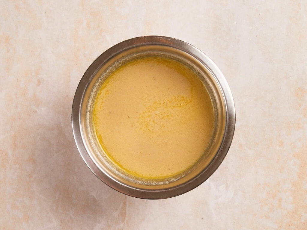 A stainless steel bowl filled with a light brown, smooth liquid mixture.