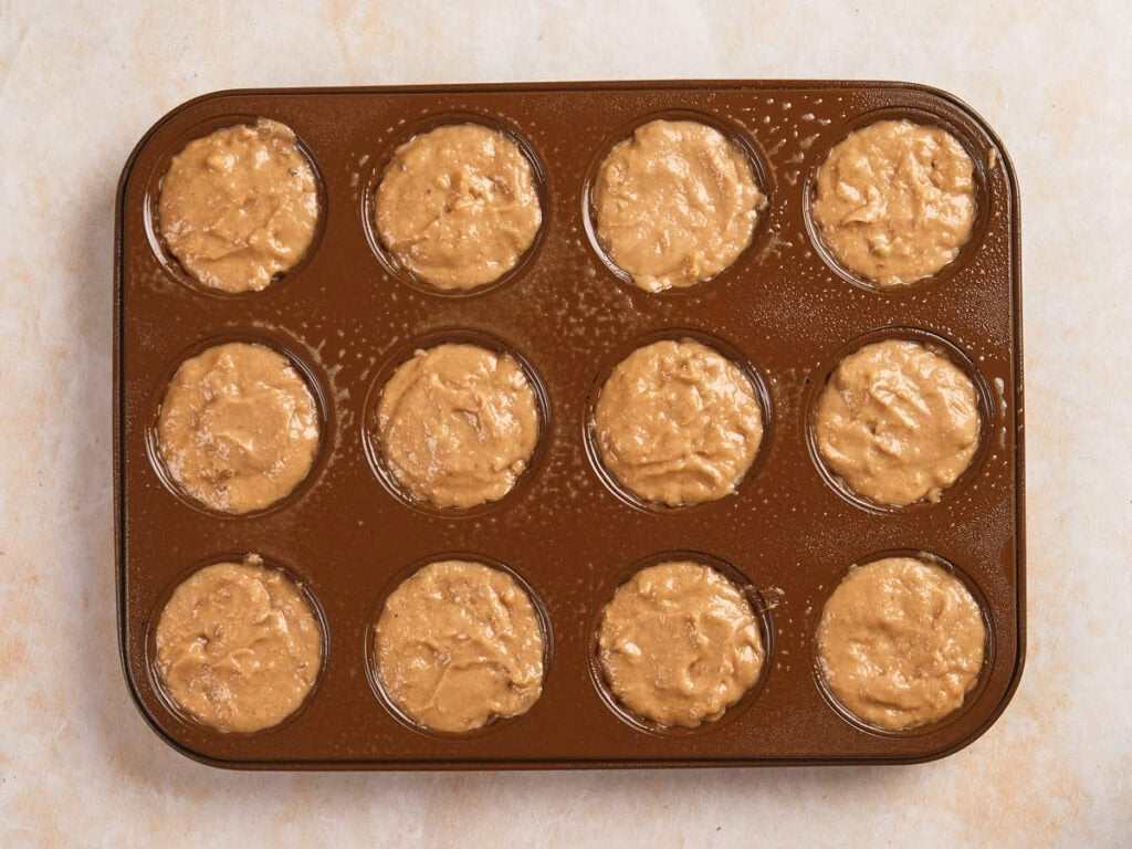 A muffin tin with twelve wells filled with raw muffin batter, ready to be baked.