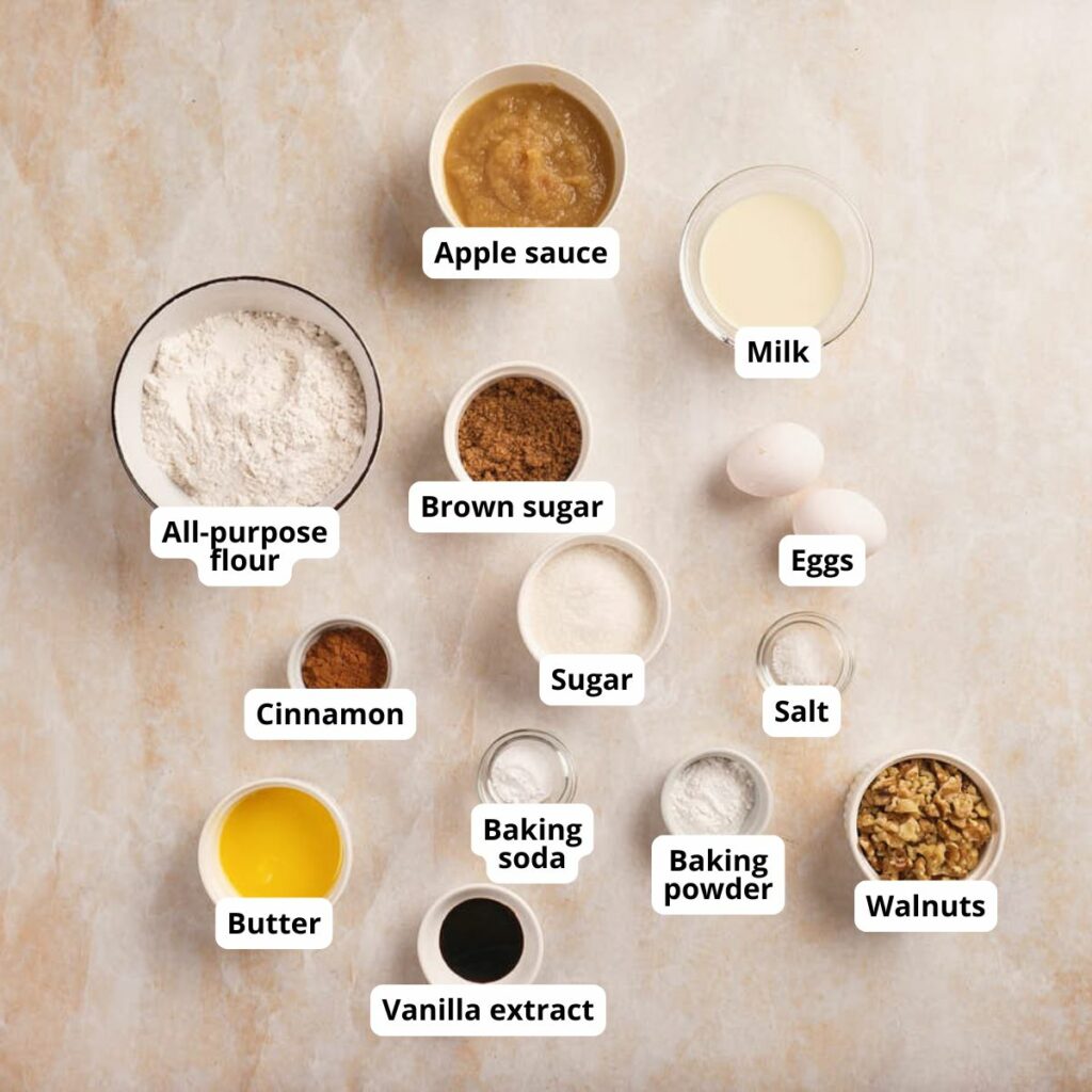 A flat lay of labeled baking ingredients for applesauce muffins on a light-colored surface.