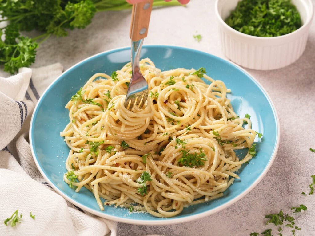 A plate of spaghetti garnished with chopped parsley and parmesan cheese, with a fork twirling the pasta.