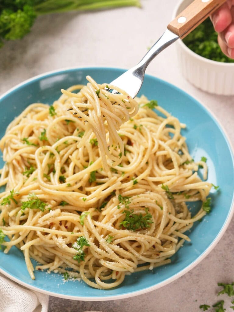 A spaghetti garnished with chopped parsley, with a fork lifting a portion of the pasta.