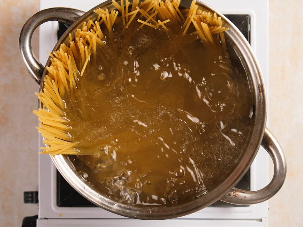 A pot of spaghetti is partially submerged and cooking in boiling water on a stove top.