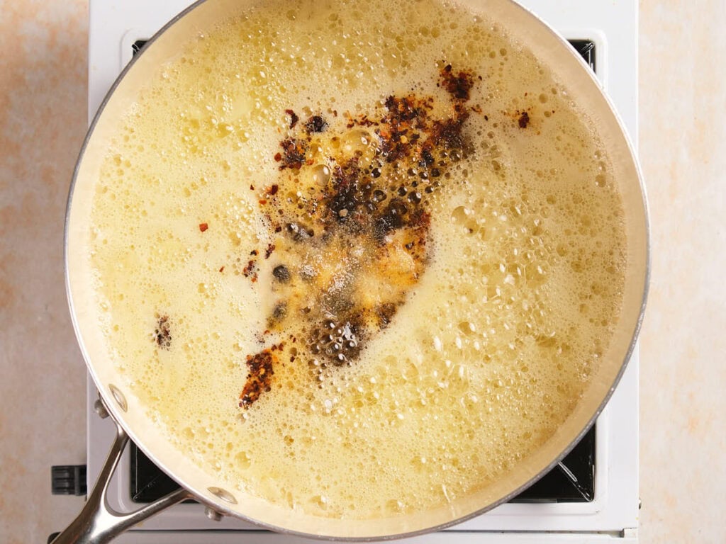 A frying pan on a stove with bubbling melted butter and spices.