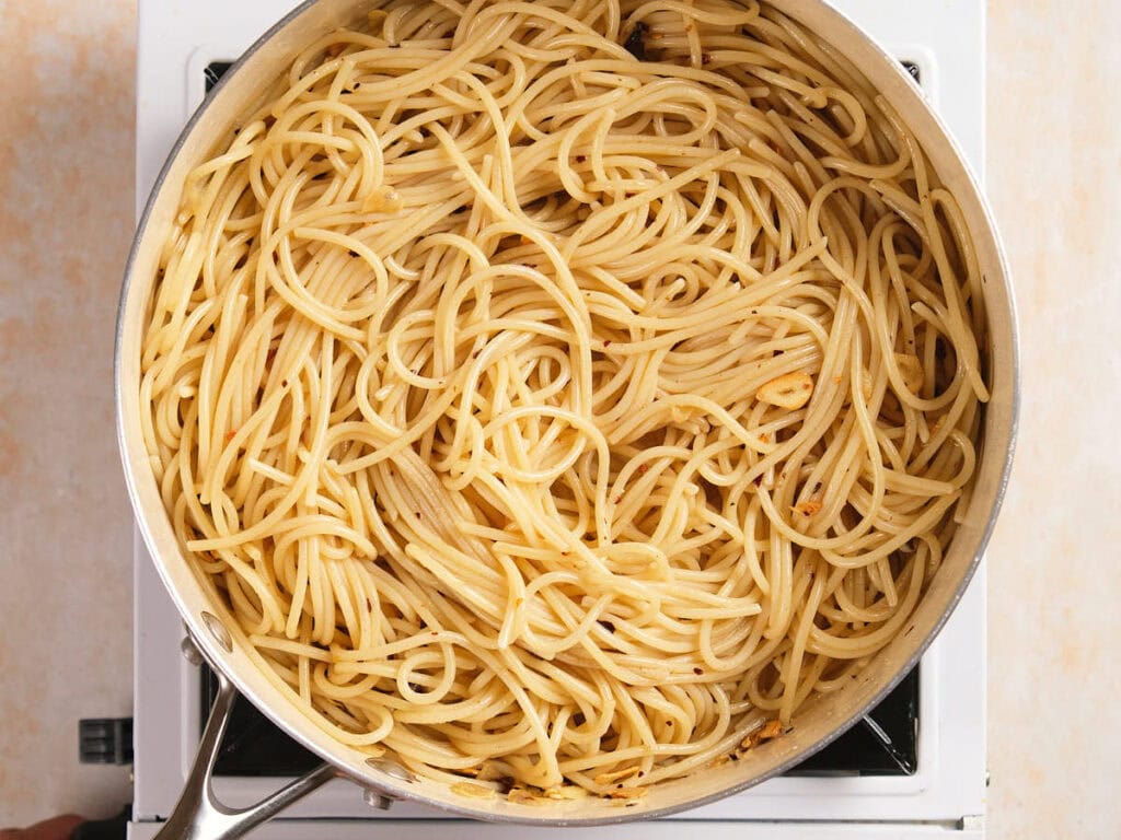 A pot of cooked plain spaghetti noodles, lightly coated with oil or sauce, sits on a stovetop burner.
