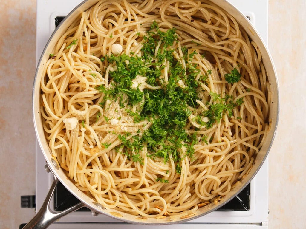 A pan of cooked spaghetti topped with chopped parsley and parmesan cheese.