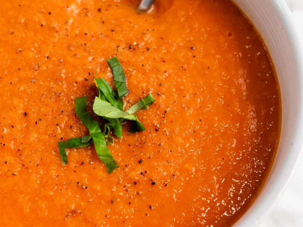 Close-up of a bowl of tomato soup garnished with chopped fresh basil and black pepper.