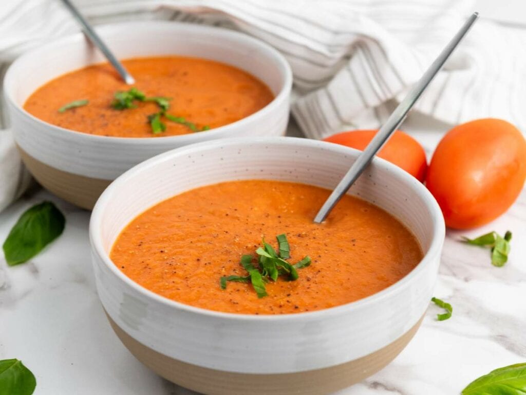 Two bowls of tomato soup garnished with chopped basil, each with a spoon.