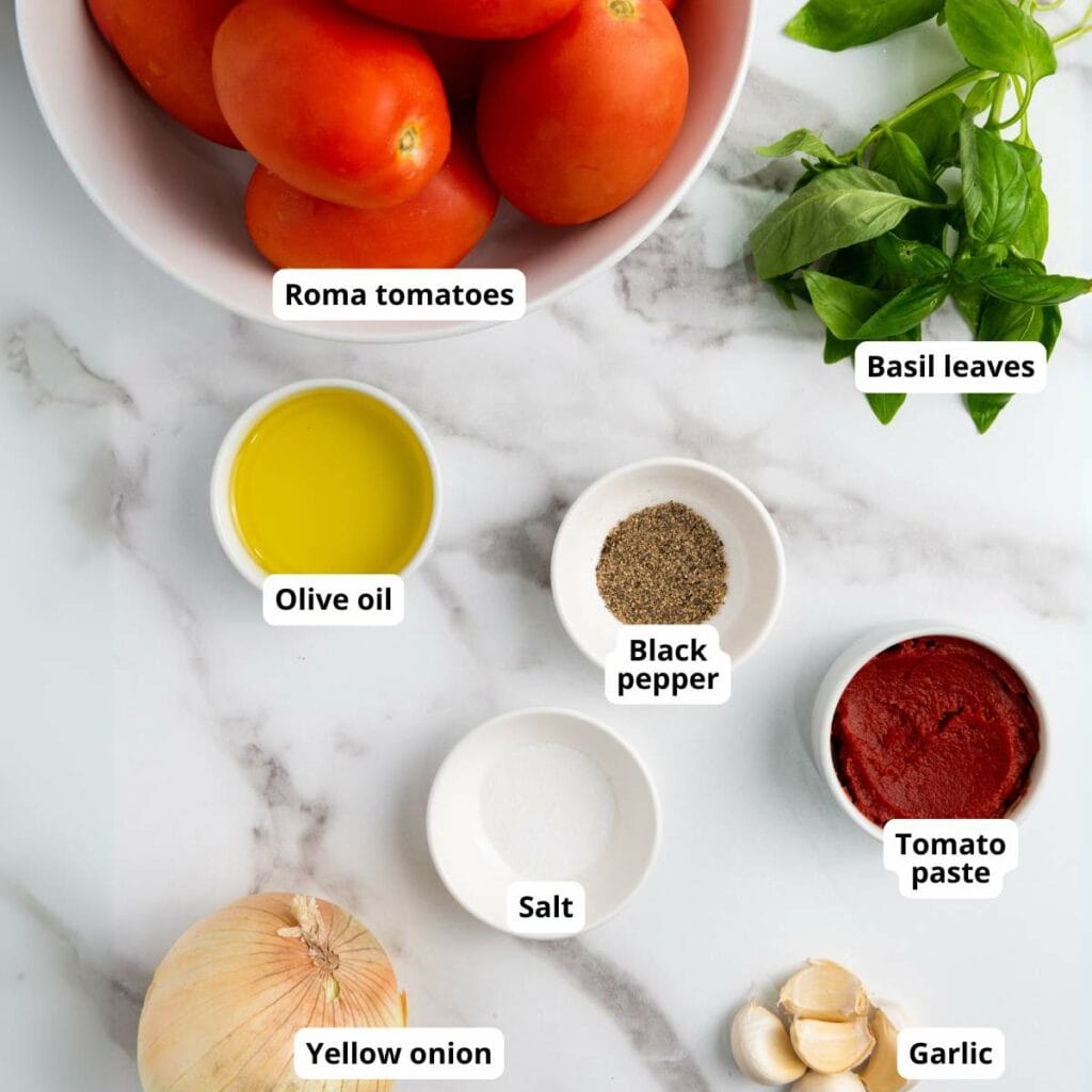 Labeled ingredients for tomato basil soup on a marble counter.