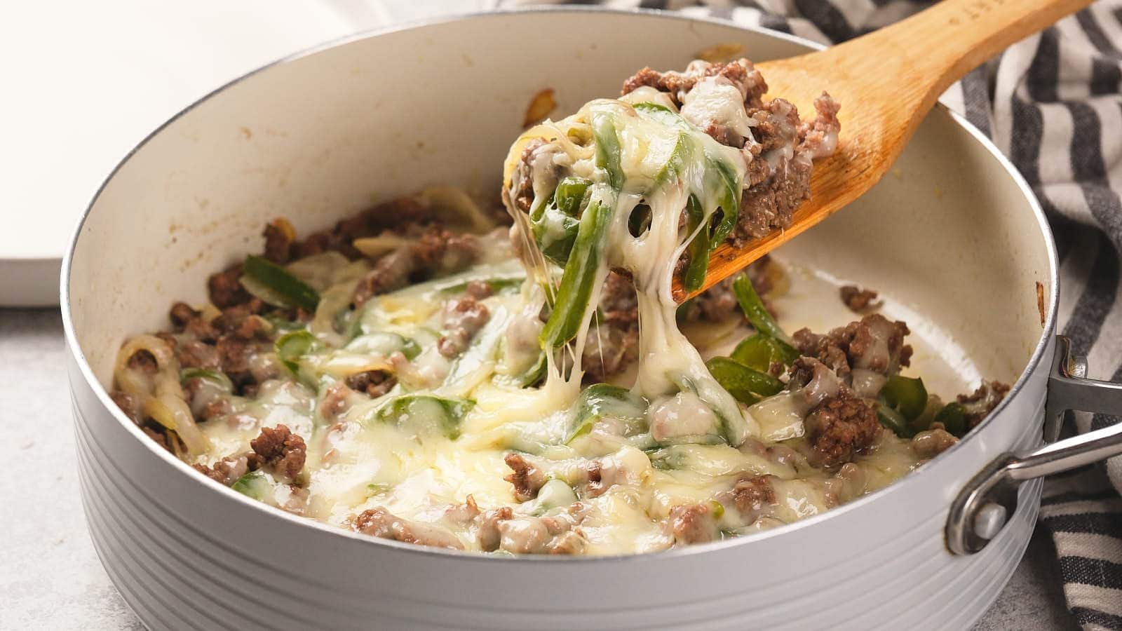 Image shows a wooden spatula cutting philly cheesesteak casserole from baking dish.