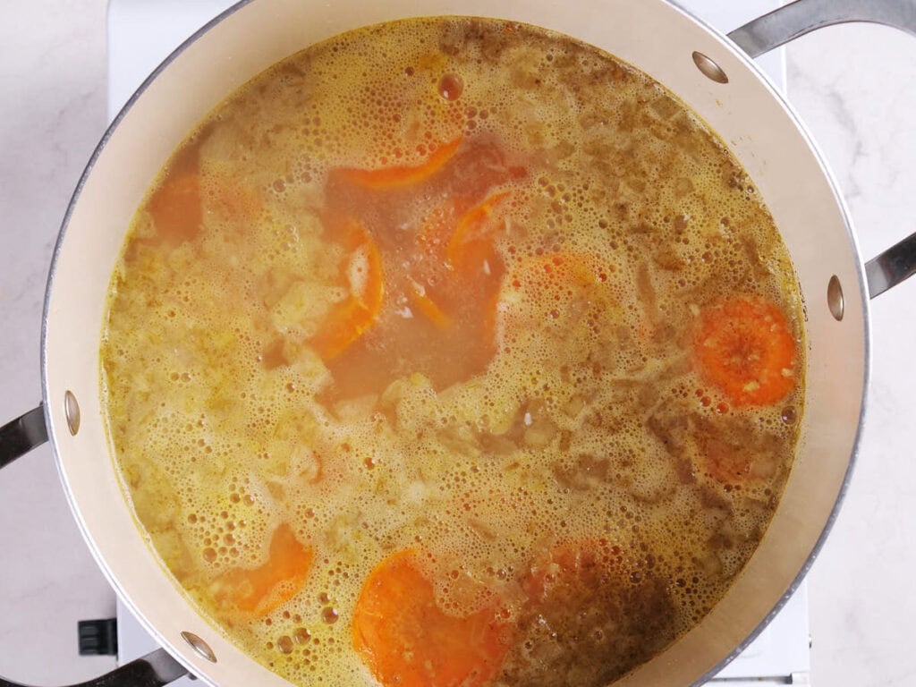 A pot of soup with visible carrots and onions simmering on a stove.