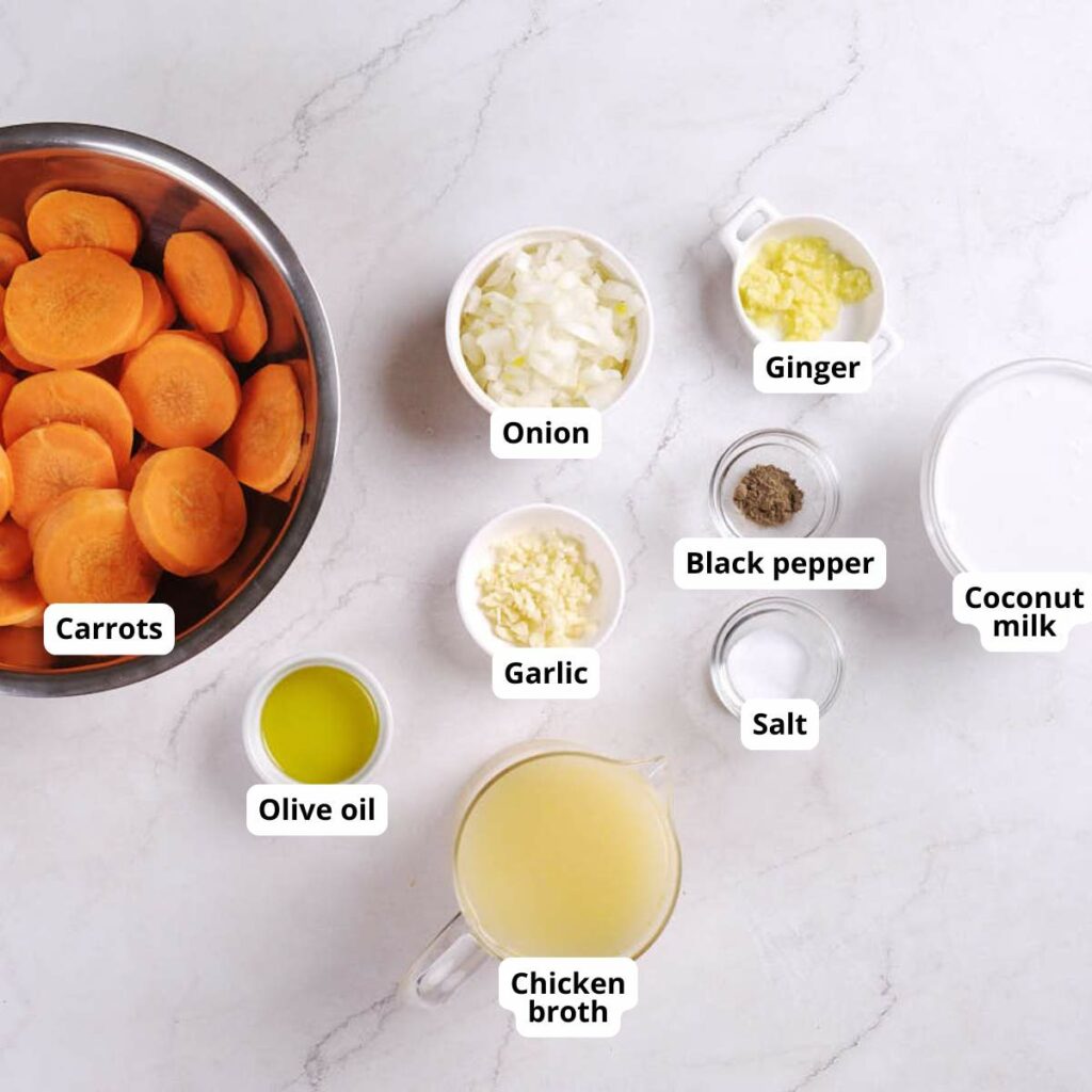 Various labeled ingredients for a carrot ginger soup recipe are arranged on a white surface.