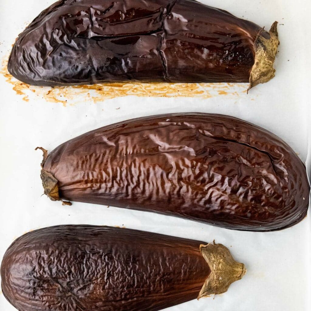 Three halves roasted eggplants with wrinkled, browned skins are arranged upside down.