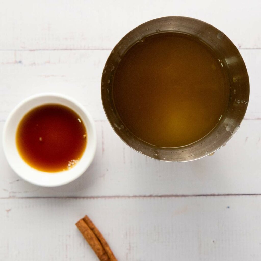 A metal container with brown liquid, a small white bowl of honey, and a cinnamon stick.