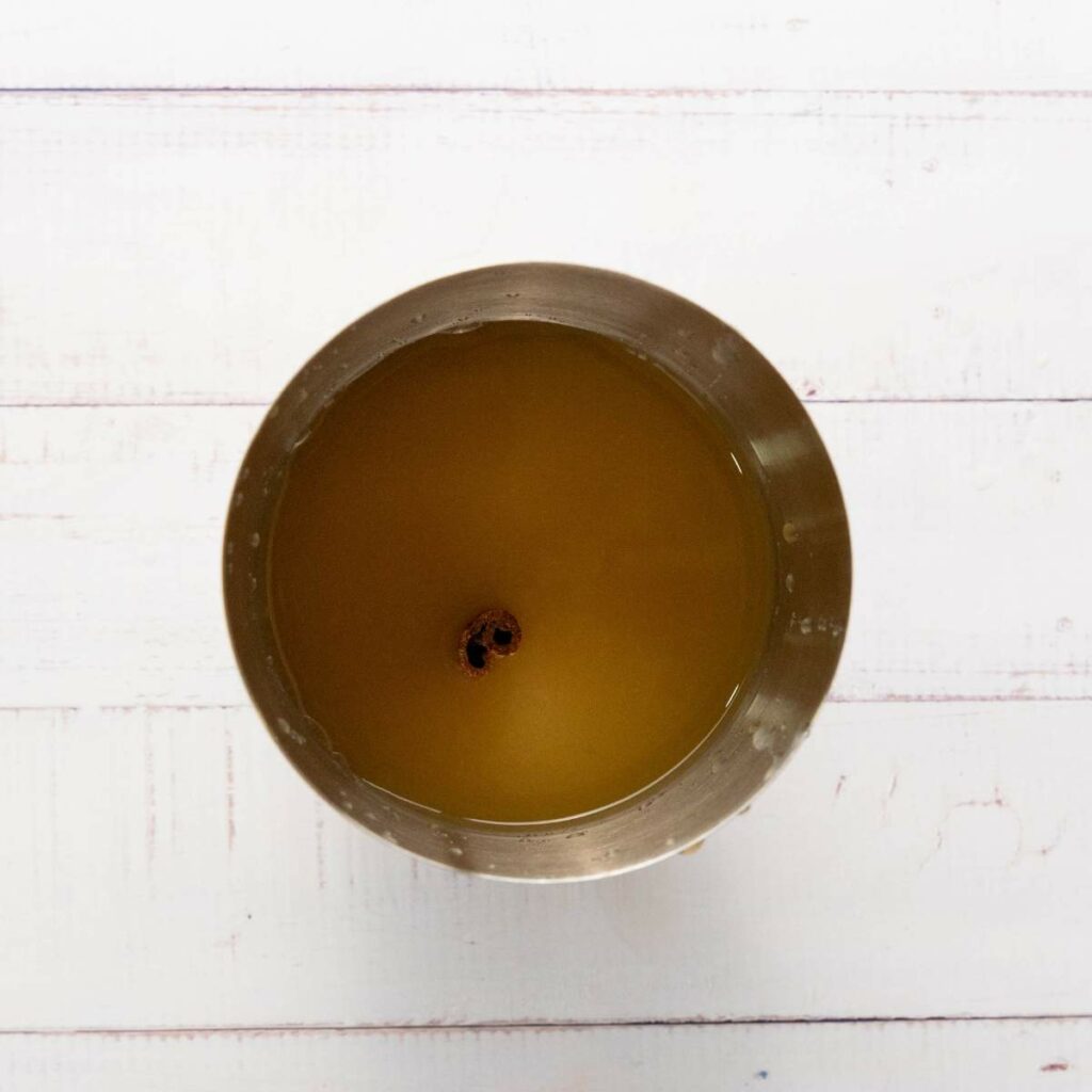 A stainless steel cup filled with yellowish liquid and a cinnamon stick floating in the center.