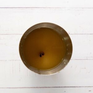 A stainless steel cup filled with yellowish liquid and a cinnamon stick floating in the center.