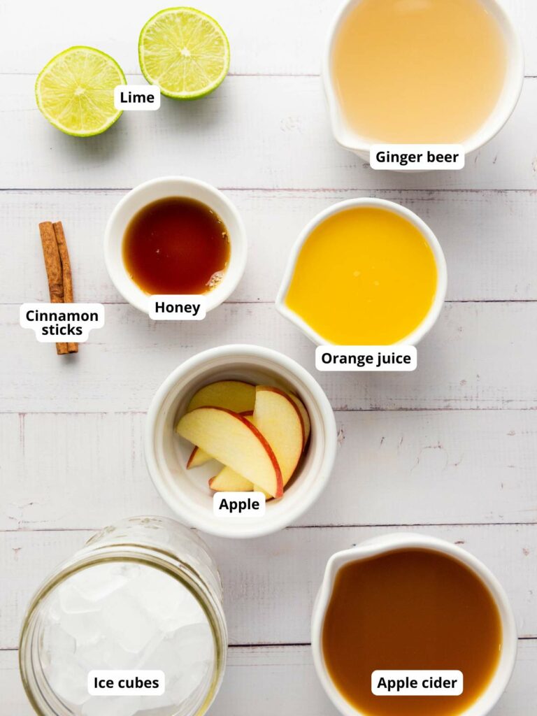 A flat lay of labeled ingredients for fall mocktail recipe on a white surface.