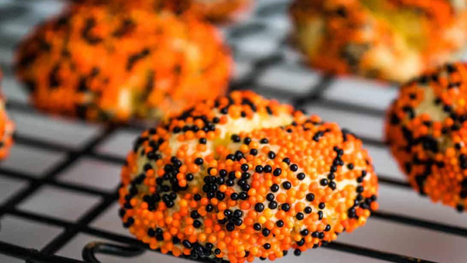 Some orange and black sprinkled cookies on a cooling rack.
