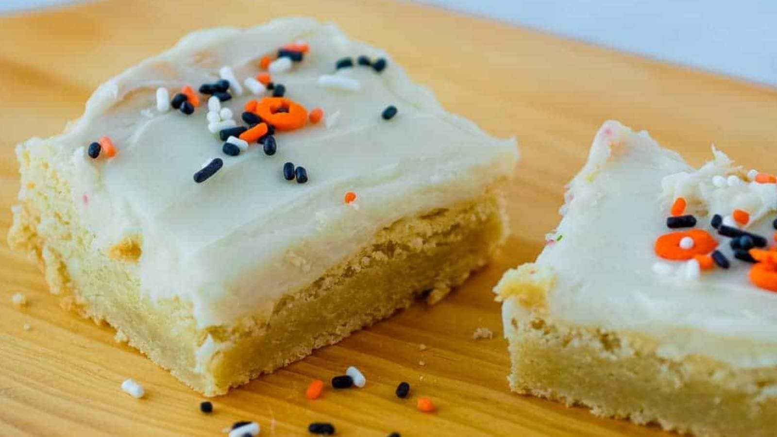 Two sugar cookie bars with sprinkles on a wooden cutting board.