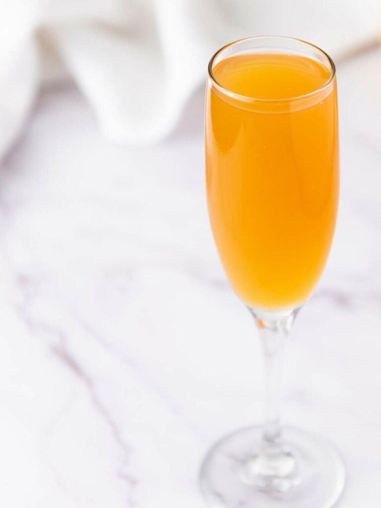 A champagne flute filled with orange-colored liquid on a light marble surface.
