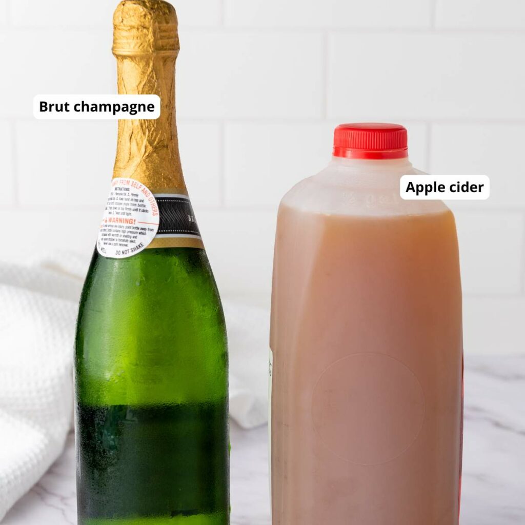 A bottle of brut champagne next to a plastic jug of apple cider, both labeled, on a white surface.