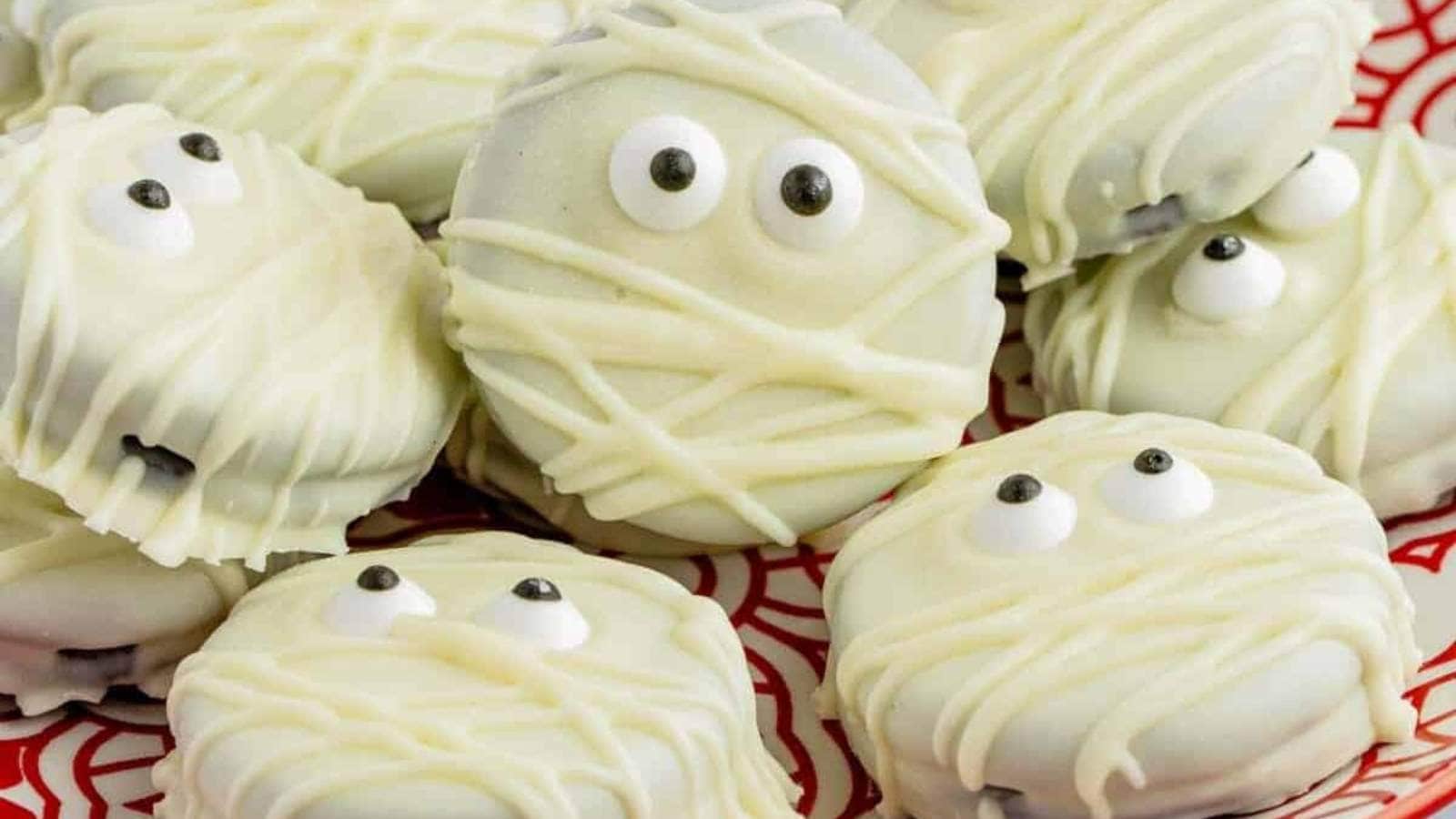 Mummy cookies on a red plate with eyes on them.