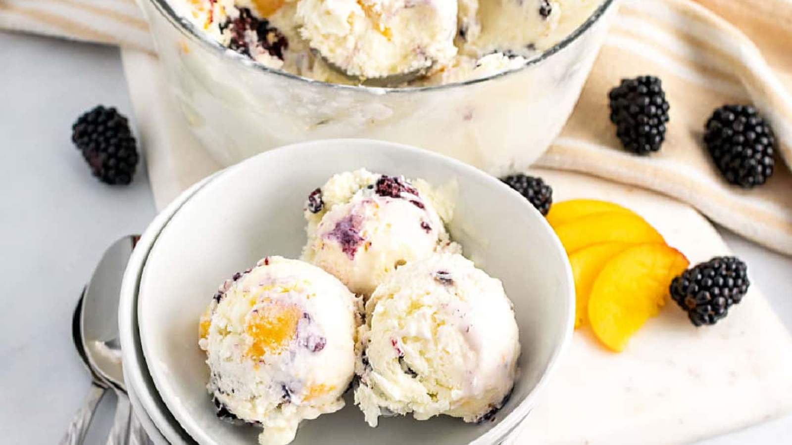 Peach and blackberry ice cream scoops in white bowls.
