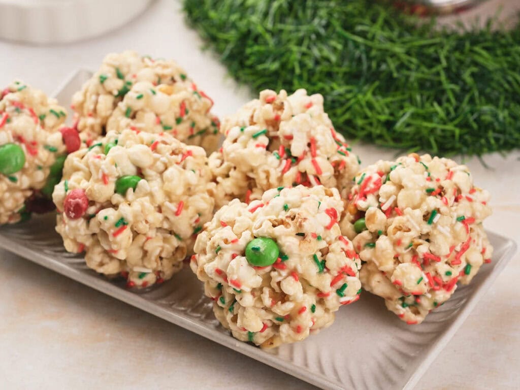 A rectangular plate with popcorn balls coated in sprinkles and m&m's chocolate pieces.